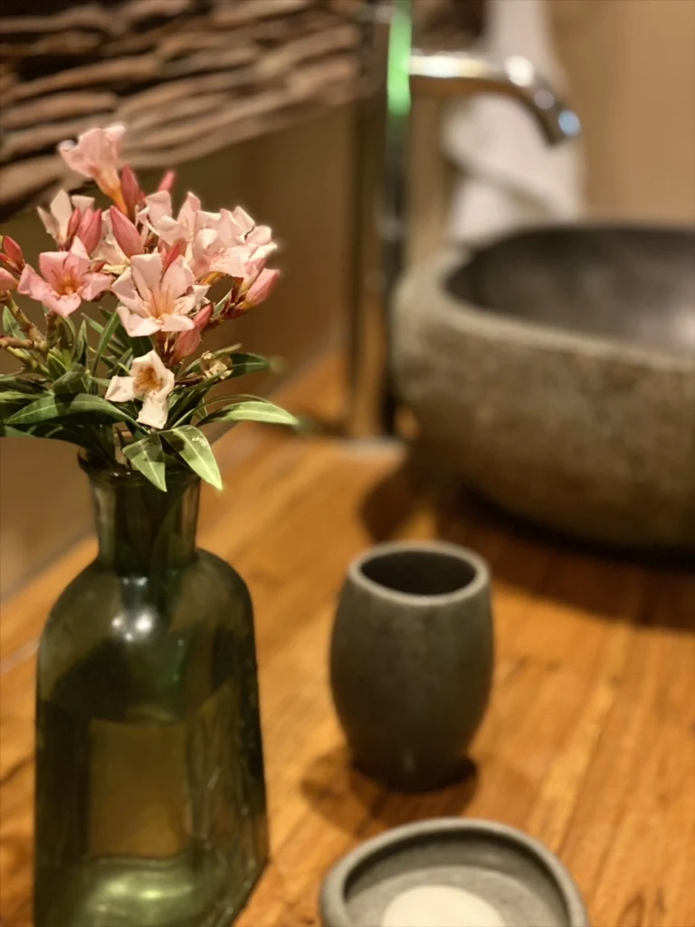 Flores junto a un lavabo de piedra y superficies de madera cálida.