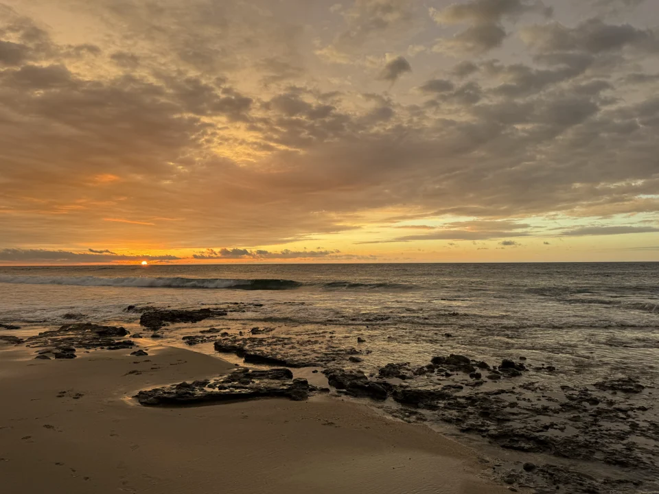 Atardecer anaranjado sobre el océano y la orilla rocosa.