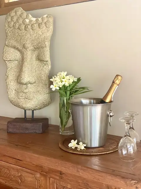 Botella en una cubitera con copas, flores y un rostro tallado en piedra.