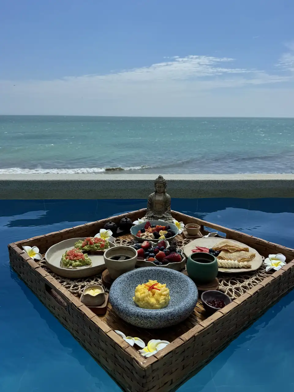 Platos de desayuno en una bandeja flotante en una piscina frente al océano.