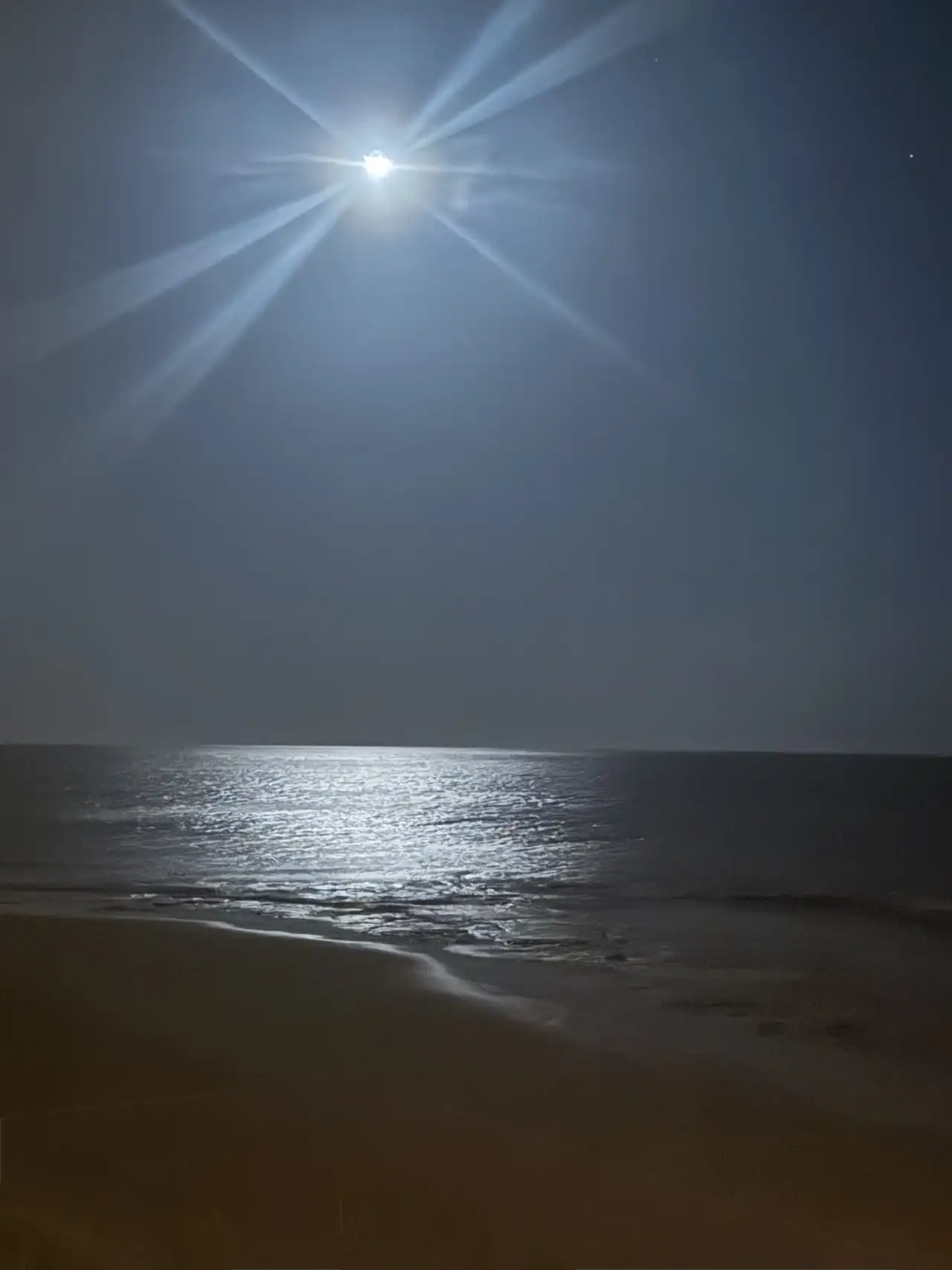 Luz de luna reflejada en el océano junto a una playa de arena oscura.