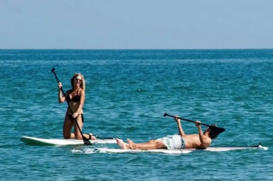 Dos personas con remos sobre tablas en el mar.