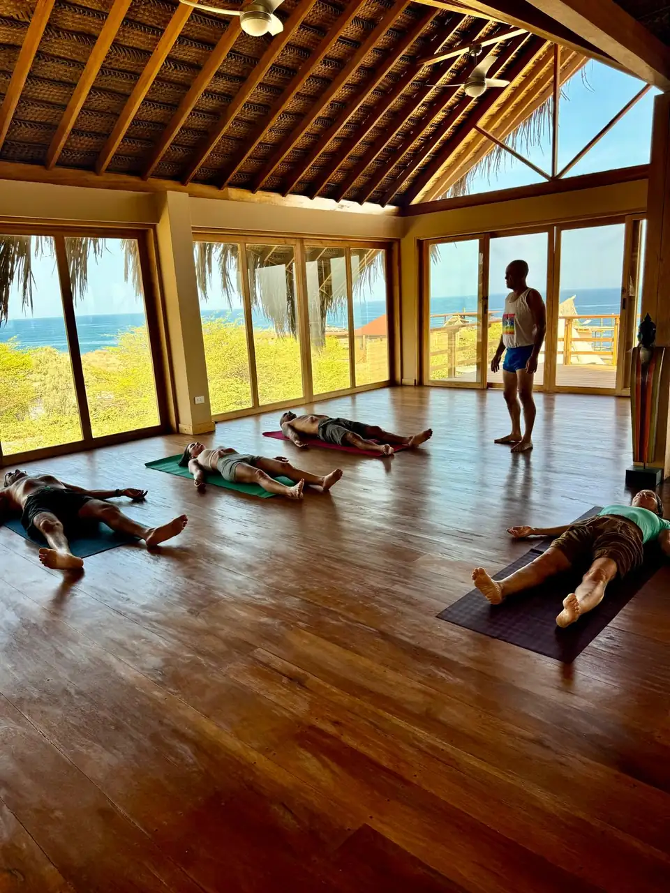 Personas descansando sobre esterillas de yoga en una sala frente al mar.
