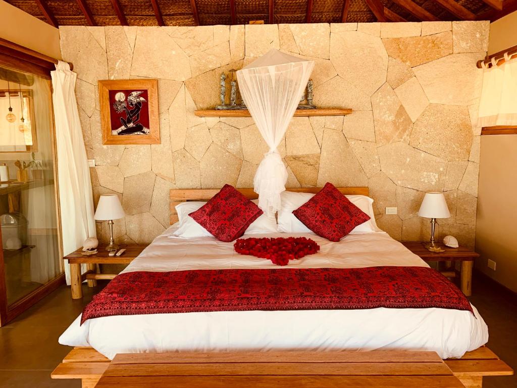 Dormitorio de El Encanto con cojines rojos, mosquitero y un corazón de pétalos de rosa sobre la cama.